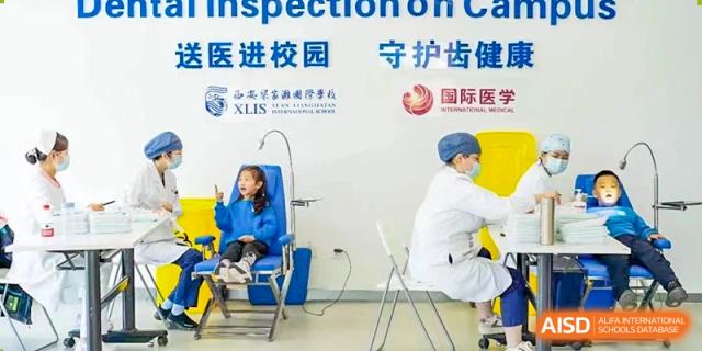 A young student from Xi'an Liangjiatan International School sits in a chair receiving a check-up from a medical professional, with a sign in Chinese visible in the background.