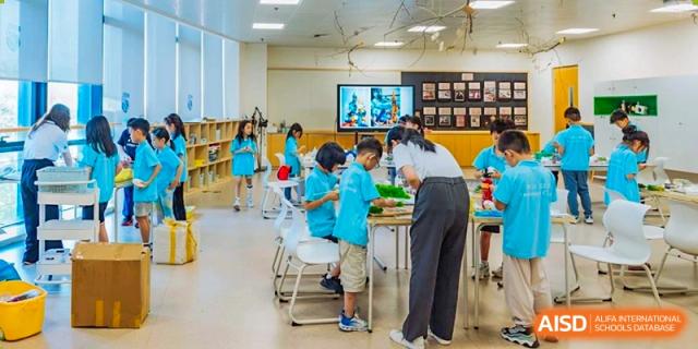 A teacher at Xi'an Liangjiatan International School works with two young students on a project at a table in a bright classroom.