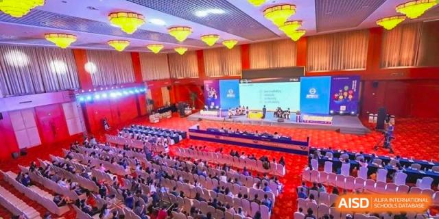 A large group of educators and attendees from Xi'an Liangjiatan International School sit in a brightly lit auditorium for a conference or professional development seminar.