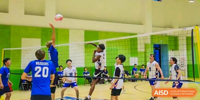 Two students from Xi'an Liangjiatan International School are at the net, jumping to block a ball during a volleyball game in the school gymnasium.