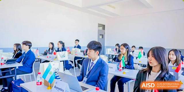 A male Xiamen International School student in a suit jacket working on a laptop at a table with other students.