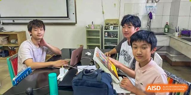 Two Xiamen International School students working together and looking at books or materials on a desk.