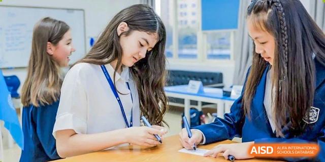 A female Xiamen International School student with long hair writing notes at a table in a bright study area.