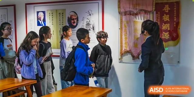 A Xiamen International School staff member interacting with two young male students in a hallway.