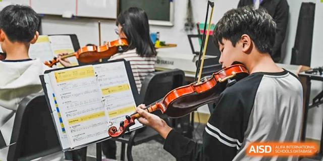 An Xiamen International School student playing the violin during a musical performance, with sheet music visible.