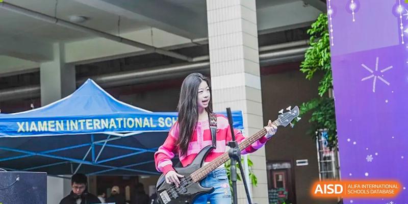 A female Xiamen International School student passionately playing an electric bass guitar during a performance.