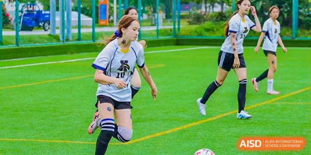 A female Xiamen International School student playing football on a grassy pitch during a match.