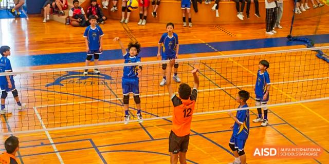 Xiamen International School students playing a game of volleyball on an indoor court, with a student jumping at the net.