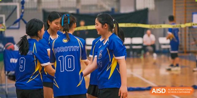 Two female Xiamen International School students in blue and yellow sports uniforms talking on the court during a game.