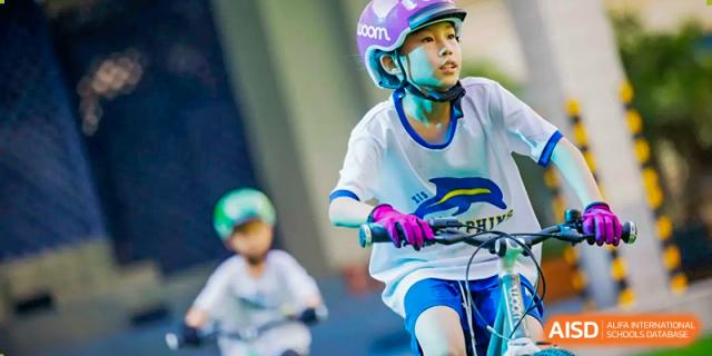 A young Xiamen International School student wearing a helmet and protective gear while riding a scooter or skates.