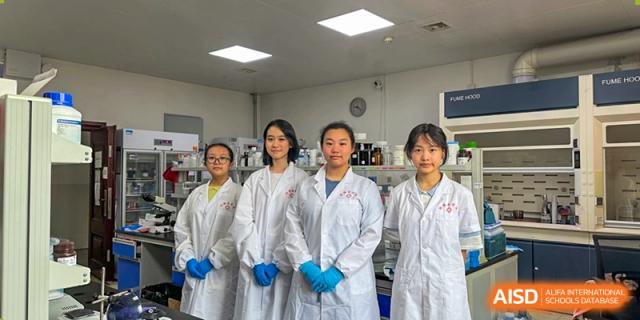 A group of Yali High School International Department female students in lab coats and gloves posing in a science laboratory.