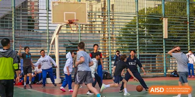 Students play a game of basketball on an outdoor court with a chain-link fence at Yali High School International Department.