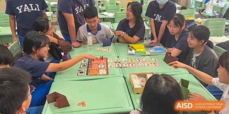 Students and an adult are seated at a table playing a board game during a club or activity session at Yali High School International Department.