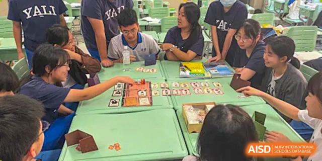 Students and an adult are seated at a table playing a board game during a club or activity session at Yali High School International Department.