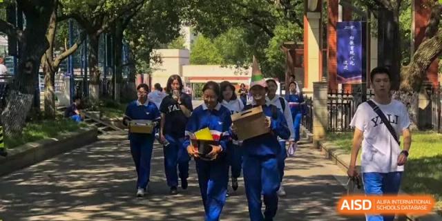 A group of students in blue uniforms walks together outdoors on the campus, with some carrying boxes, at Yali High School International Department.