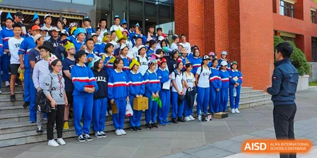 Group photo of Yali High School International Department students in blue and white uniforms standing outside a red-brick building.