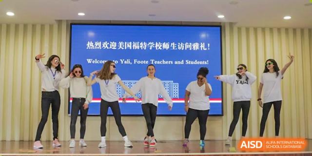 Four dancers on a stage performing for Yali High School International Department students and teachers, with a banner in Chinese and English welcoming them.