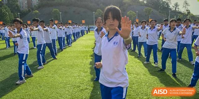 Yali High School International Department female student in a white and blue uniform practicing an outdoor exercise or martial arts pose on a field.