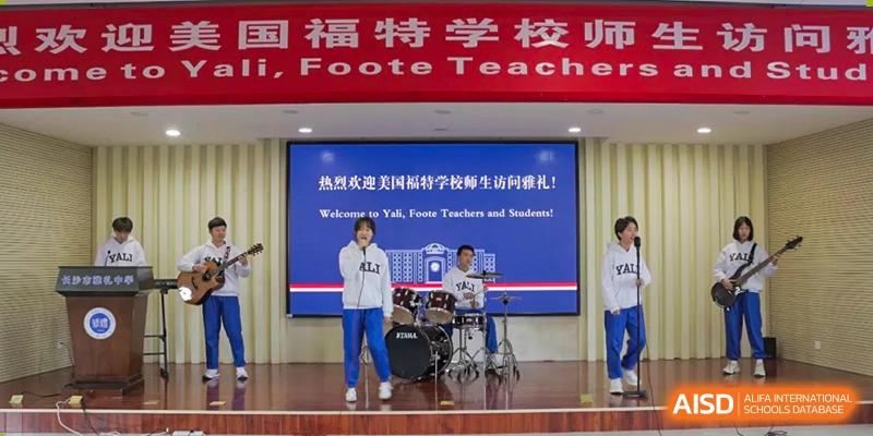 A Yali High School International Department student performing on a drum set on stage with a welcome banner for Foote Teachers.