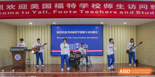 A Yali High School International Department student performing on a drum set on stage with a welcome banner for Foote Teachers.