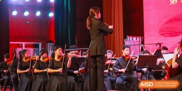 A conductor, likely of the Yali High School International Department orchestra, directing musicians during a performance.