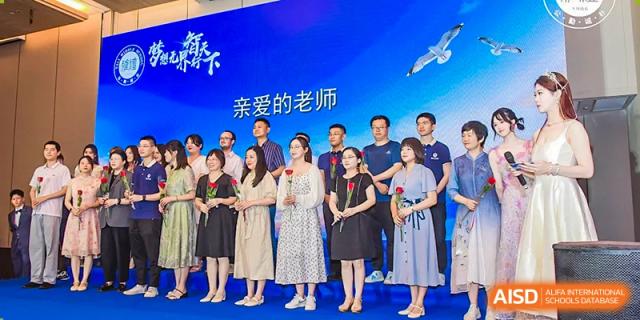 Yali High School International Department teachers posing for a group photo on a stage with a banner that says '亲爱的老师' (Dear Teachers).