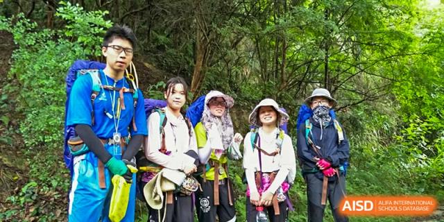 Yali High School International Department students in harnesses and safety gear during an outdoor adventure activity in a forest.