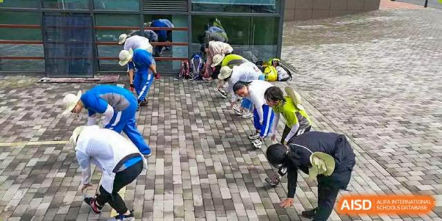 Yali High School International Department students or staff preparing for a climbing or outdoor activity, bending over to adjust their gear.