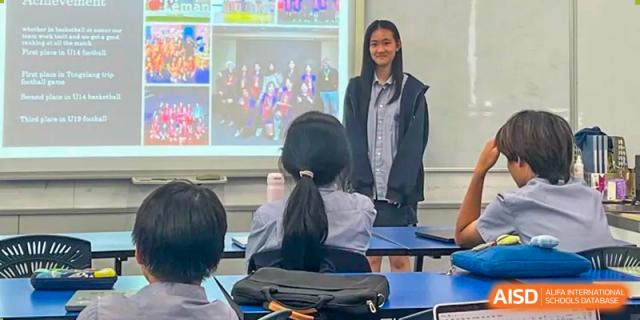 A female student at Yew Chung International School of Qingdao giving a presentation in front of a class with a large projected screen.