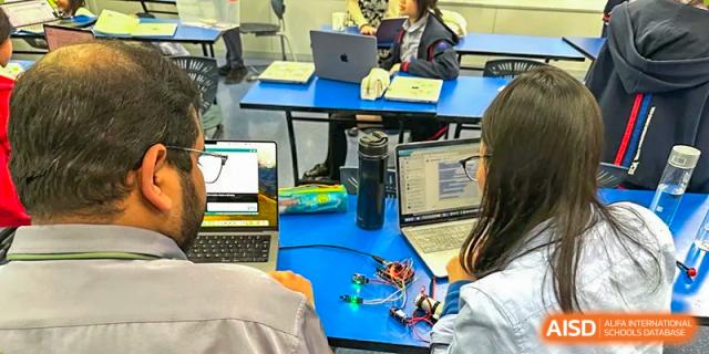 Students at Yew Chung International School of Qingdao working on STEM or coding projects with laptops and building blocks on a bright blue table.