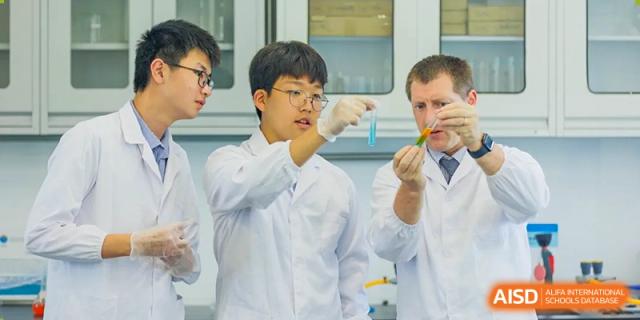 A male student at Yew Chung International School of Qingdao in a lab coat, holding a small object with tongs during a science experiment.