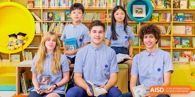 A diverse group of students at Yew Chung International School of Qingdao seated together in a bright area, possibly a library or reading space.