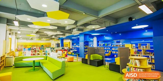 An interior view of the modern, colorful library or media center at Yew Chung International School of Qingdao with green and blue seating areas.