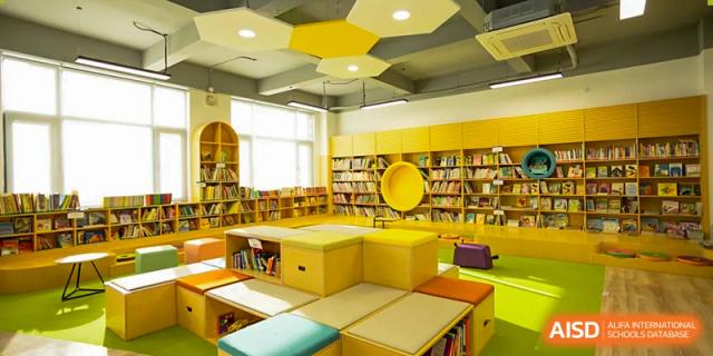 An interior view of the brightly colored library and learning resource center at Yew Chung International School of Qingdao, featuring yellow shelving and seating.