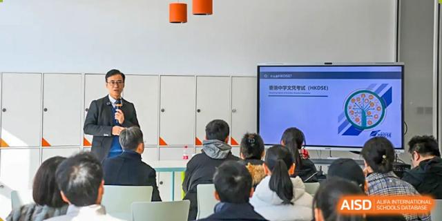Students at Yew Chung International School of Qingdao seated in a classroom, looking at a presentation on a large digital whiteboard.