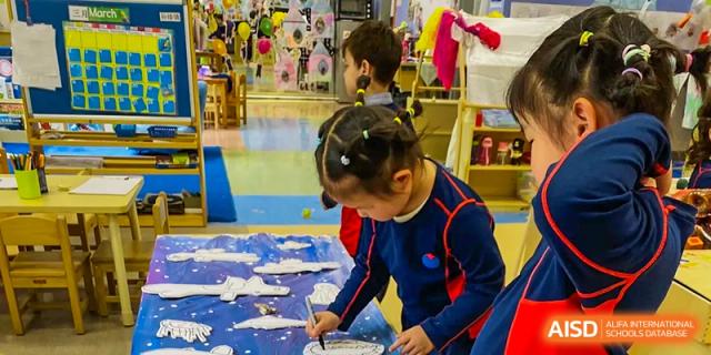 A young student at Yew Chung International School of Qingdao concentrating on a hands-on art project, painting a background with blue and white.