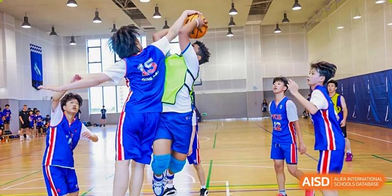 Two students at Yew Chung International School of Qingdao competing for the ball during an intense moment of an indoor basketball game.