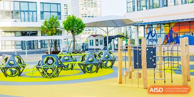 An outdoor play area at Yew Chung International School of Qingdao featuring sun shades and brightly colored tricycle-style bikes.