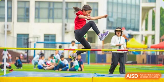 A female student at Yew Chung International School of Qingdao performing a high jump over a bar during an outdoor track and field event.