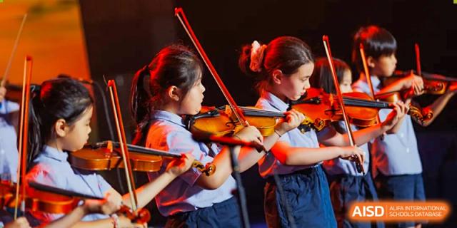 Two young female students at Yew Chung International School of Qingdao focused on playing the violin during a music practice session or performance.