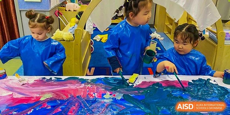 A young student at Yew Chung International School of Qingdao engaged in a messy, hands-on art project, surrounded by bright paint.