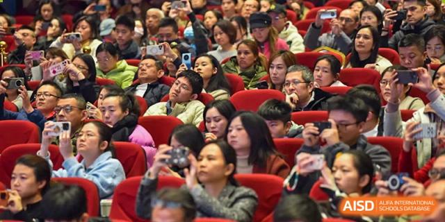 A large audience of students and parents at Yew Chung International School of Qingdao seated in an auditorium, attending an event or performance.