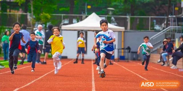 A male student at Yew Chung International School of Qingdao running a race on an outdoor track in a blue and yellow sports uniform.