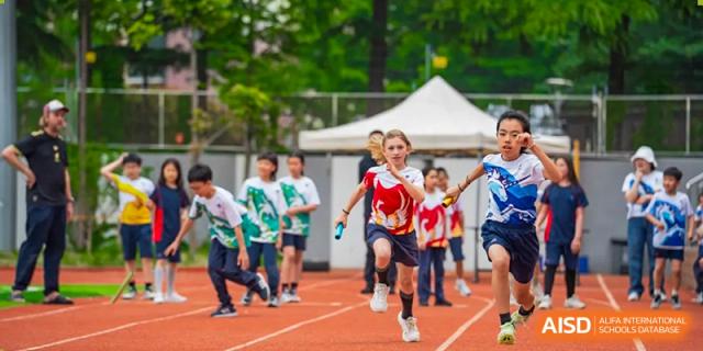 A student at Yew Chung International School of Qingdao running a relay race, handing off a baton on an outdoor track.