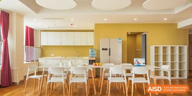 An interior view of a bright, modern kitchen and dining area at Yew Chung International School of Qingdao, featuring white cabinets and a large table.