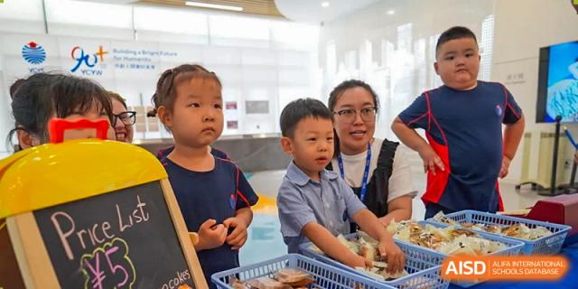 Two young male students at Yew Chung International School of Qingdao looking at items in a basket, assisted by a female staff member.