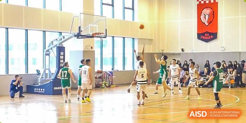 Basketball game in progress at Yew Wah International Education School of Zhejiang Tongxiang gym with players in green and white uniforms.