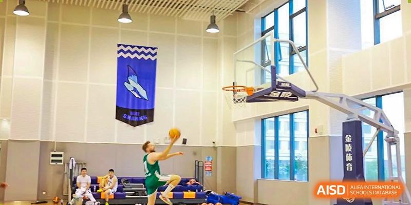 Yew Wah International Education School of Zhejiang Tongxiang student in green jersey jumping to shoot a basketball during an indoor game.