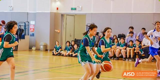 Female students from Yew Wah International Education School of Zhejiang Tongxiang in green uniforms dribbling basketballs during a game or practice session.