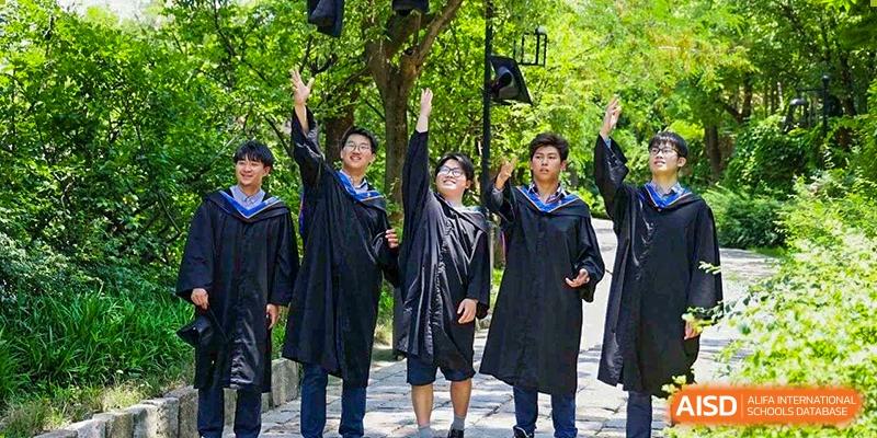 Three graduating students from Yew Wah International Education School of Zhejiang Tongxiang in caps and gowns celebrating outdoors.